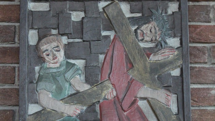 Relief an Ziegelmauer zeigt zwei Figuren, eine mit Kreuz.