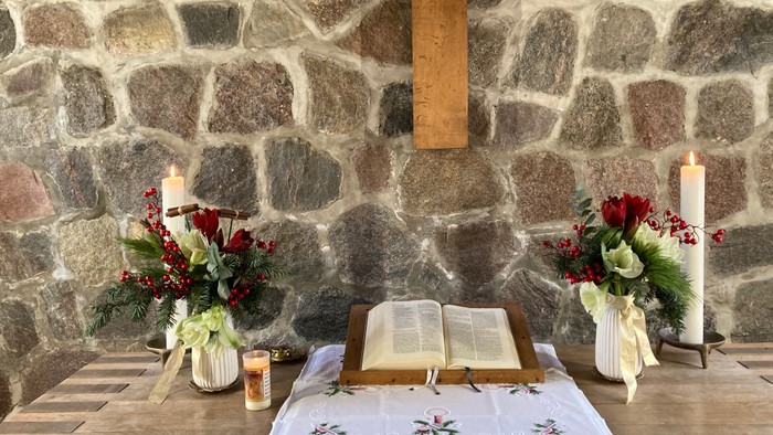 Ein Tisch mit offenem Buch, Kerzen und Blumen vor einer Steinwand