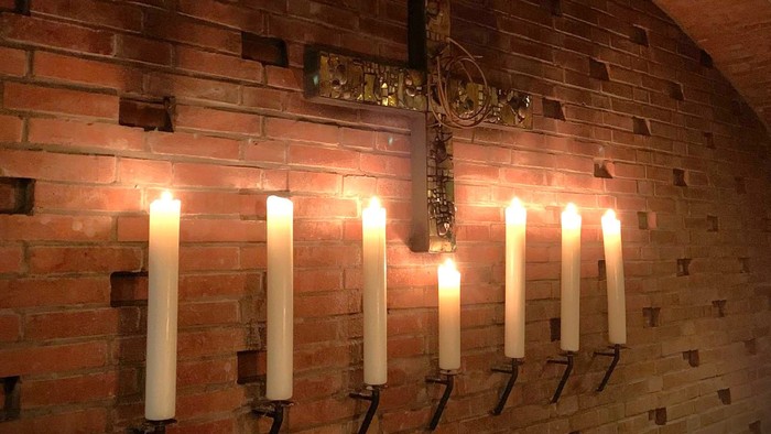 Brennende Kerzen vor einem Kreuz an einer Ziegelwand