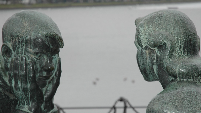 To bronzestatuer af mænd i eftertænksom samtale, vendt mod hinanden.