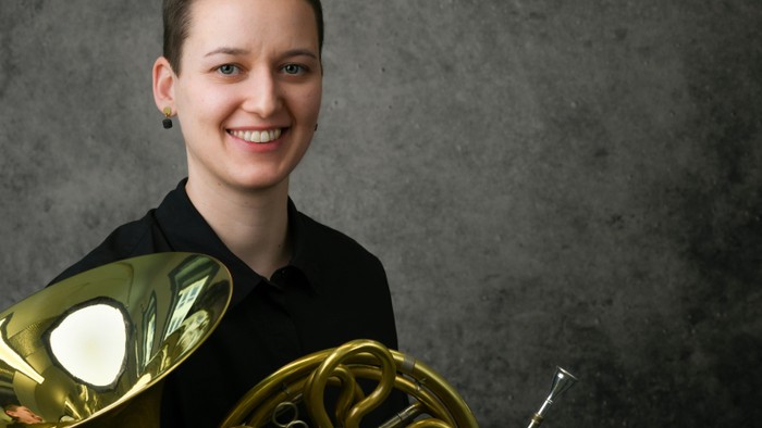 Eine Person, die lächelnd ein Waldhorn hält.