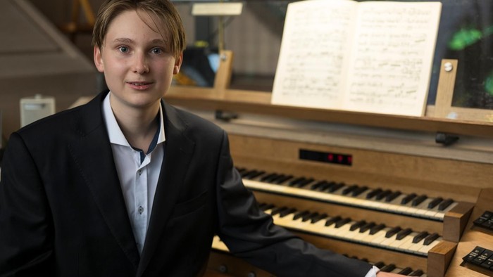 Eine Person im Anzug spielt eine Orgel mit aufgeschlagenen Noten vor sich.