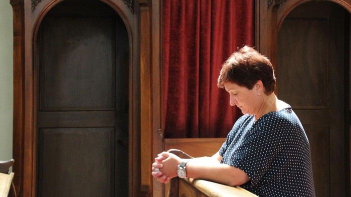 Frau kniet in einer Kirchenbank, die Hände zum Gebet gefaltet.