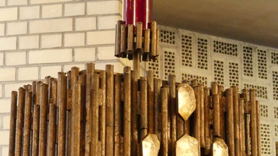 Ein hölzerner Kronleuchter mit goldenen Akzenten vor einer weißen Ziegelwand.