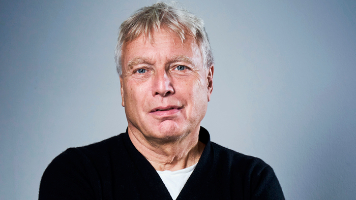 En mand i en sort sweater med et hjerte-patch står selvsikkert med armene over kors.