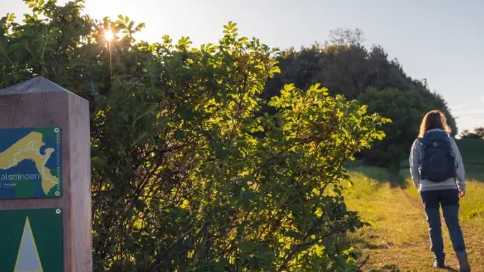 En kvinde går på en sti gennem en naturpark ved solnedgang
