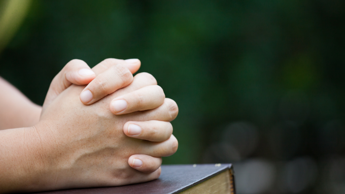 En person med sammenfoldede hænder på en bog.