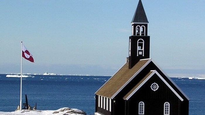 Sort kirke ved havet med dansk flag.