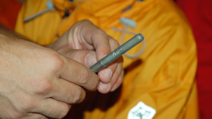 Hand hält grauen Kugelschreiber, der auf orangefarbenem Stoff liegt