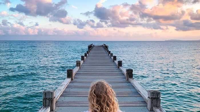 En kvinde sidder på en brygge og ser ud over havet ved solopgang