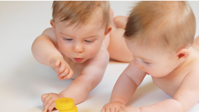 Zwei Babys spielen mit bunten Stapeltürmen auf einer hellen Oberfläche.