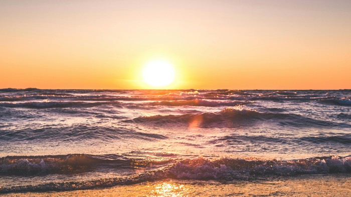 En solopgang over havet med røde og orange farver i himlen og på stranden
