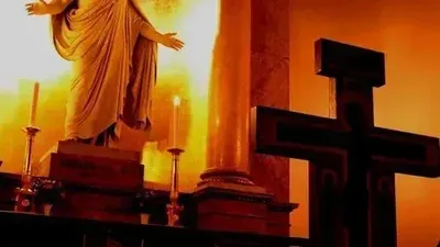 En statue af Jesus med udstrakt arme, to lysestake og et tømret kors i en kirke.