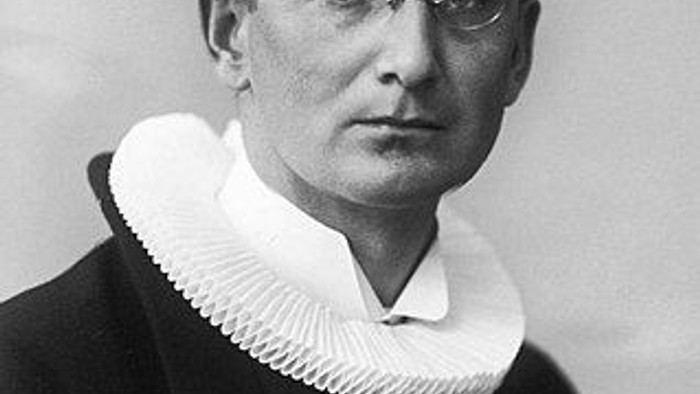 En svart og hvid fotografi af en mand med briller og hvid krage.