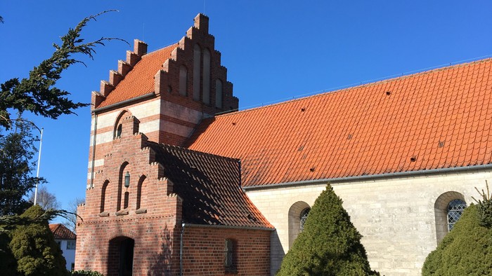 En rød murstenskirke med spids tak og et gravsted med en statue foran