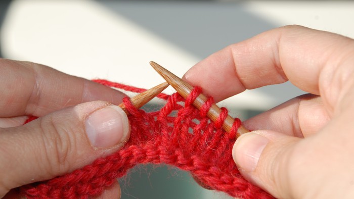 Hænder arbejder med stik i rød tråde