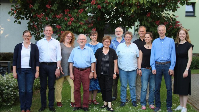 Gruppe von Menschen, die draußen in der Nähe blühender Sträucher und eines grünen Gebäudes posieren.