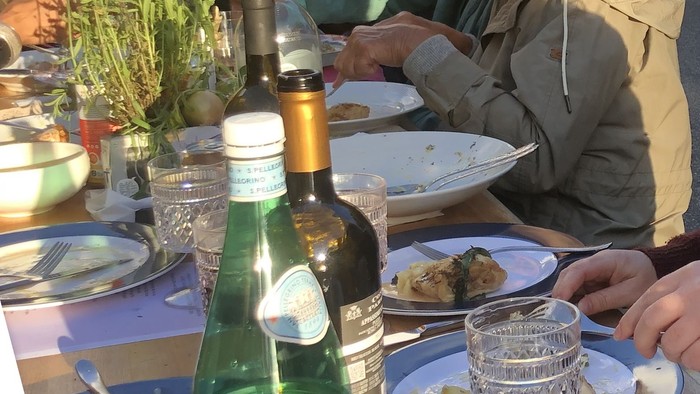 En gruppe mennesker spiser udendørs, der er stilleben og grønne flasker på bordet