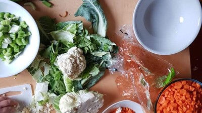 Eine Person bereitet Gemüse auf einem Tisch vor, mit verschiedenen Schalen und Messern.