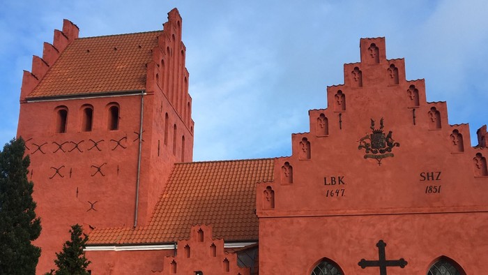 Røde kirke med tårn og gravsteder i forgrunden