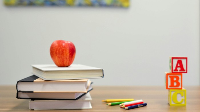 Stapel Bücher mit einem Apfel oben drauf, Buntstifte und ABC-Bauchklötze auf einem Tisch.