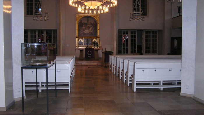 Elegante Kircheninnenausstattung mit hölzernen Kirchenbänken, Kronleuchtern und einem zentralen Altar, der mit religiösen Kunstwerken geschmückt ist.