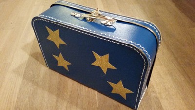 Vintage-inspireret blå kuffert med gyldne stjerneapplikationer på trægulv.