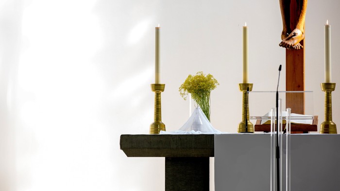 Auf einem Altar stehen zwei Kerzen, eine Vase mit gelben Blumen und eine Statue.