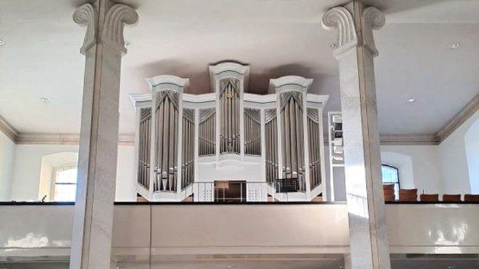 Elegante Kircheninnenausstattung mit einer großen Pfeifenorgel, die auf klassischen Säulen erhöht steht, sowie gestuften Sitzreihen und Kirchenbänken.