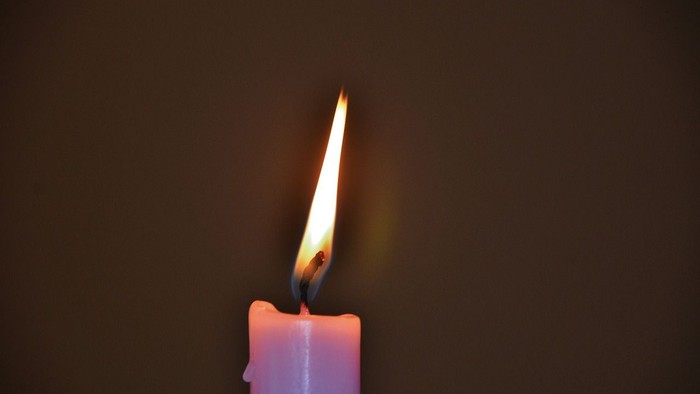 Eine brennende Kerze vor dunklem Hintergrund.
