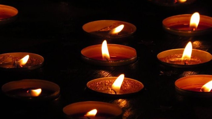 Mehrere brennende Kerzen in Metallhaltern auf dunklem Hintergrund