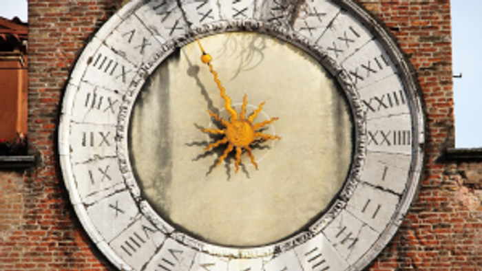 Eine verzierte astronomische Uhr mit römischen Ziffern und einem dekorativen, sonnenblumenähnlichen Design in der Mitte.