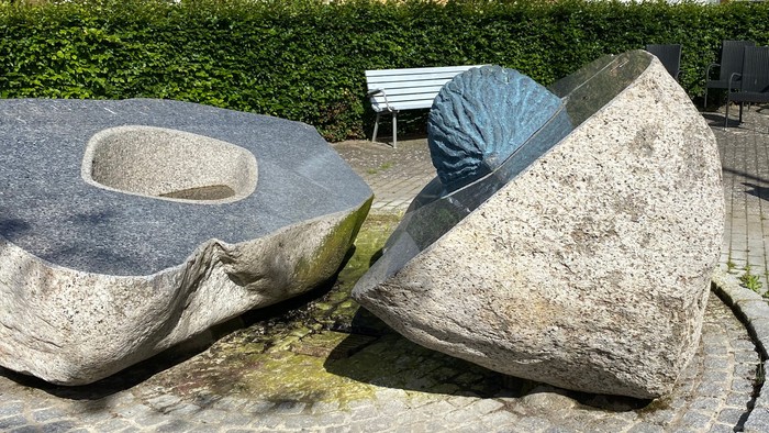 En stenskulptur i en træderne med bord og benker i baggrunden