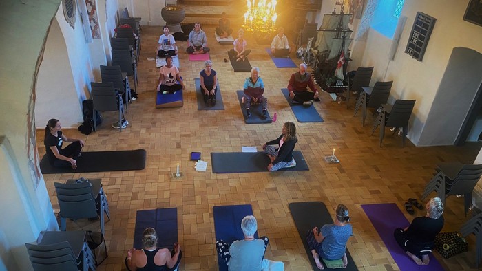 En gruppe af mennesker udfører yoga i en stor hall med høje vægge og kælderlampen.