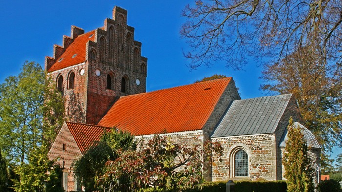 Gammel kirke med røde tag og murstensmureri i solskinn