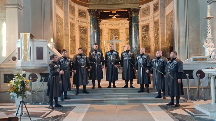 Uniformierte Musiker stehen in Formation im Inneren einer prächtigen, historischen Kirche und spielen Instrumente.