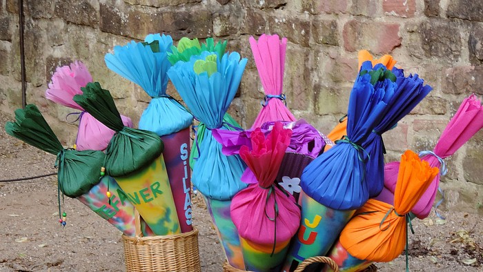 Bunte, blumengefüllte Taschen in geflochtenen Körben vor einem Ziegelwand-Hintergrund arrangiert.