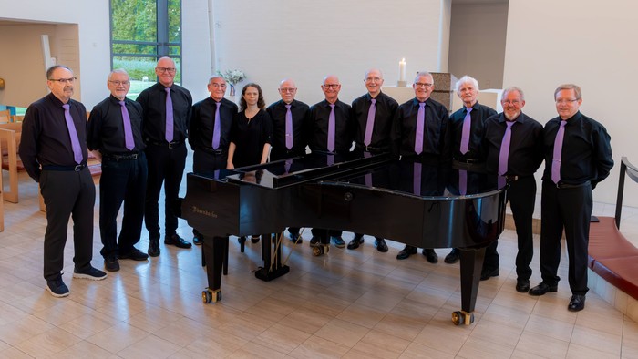 En gruppe mænd i formelt tøj med lilla slips poser sammen foran et flygel.