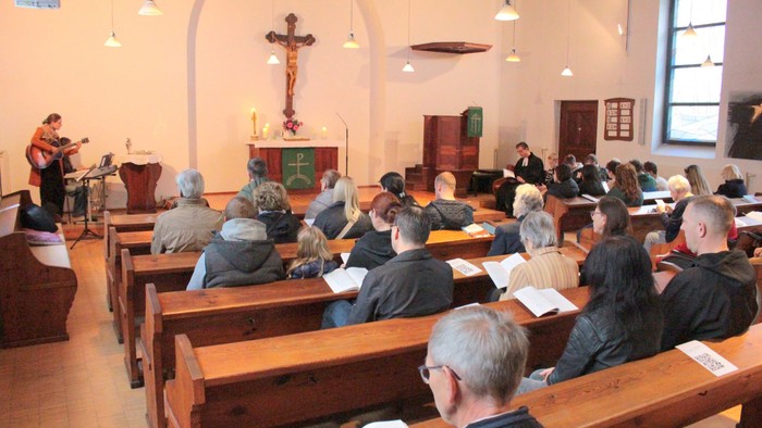 In der Kirche singt eine Gruppe Menschen, ein Mann spielt Gitarre