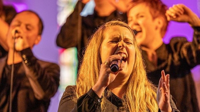 Gospelchor singt auf einer beleuchteten Bühne bei einem Gottesdienst oder Konzert.