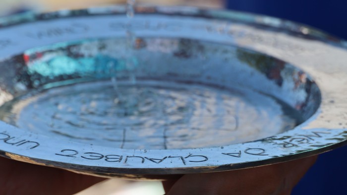 Hand hält silbernen Teller mit Wasser, auf dem 