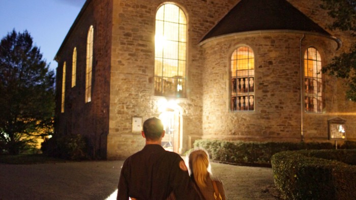 Ein Paar geht bei Nacht an einer beleuchteten Kirche vorbei