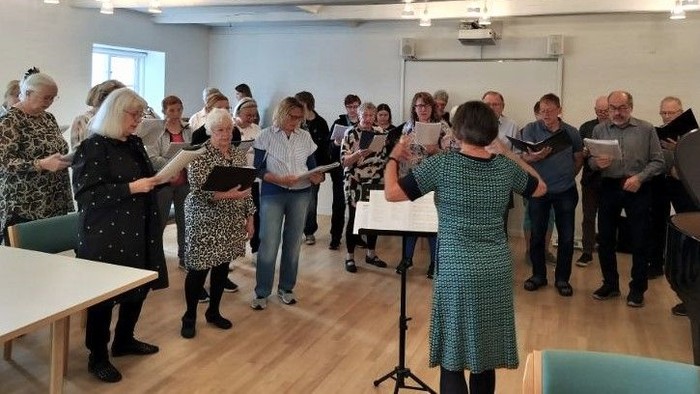 En gruppe mennesker, der synger sammen til en korprøve med noder.