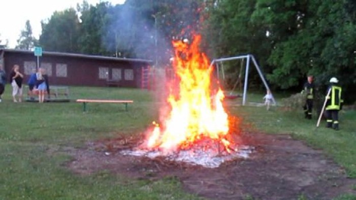 Ein Lagerfeuer auf einem Rasenplatz mit Menschen und einem Schaukelset.
