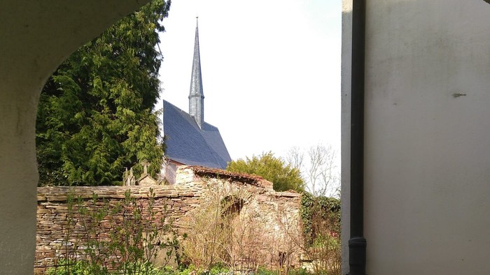 Durch den Torbogen sieht man eine Kirche mit hohem Turm und grünem Rasen.