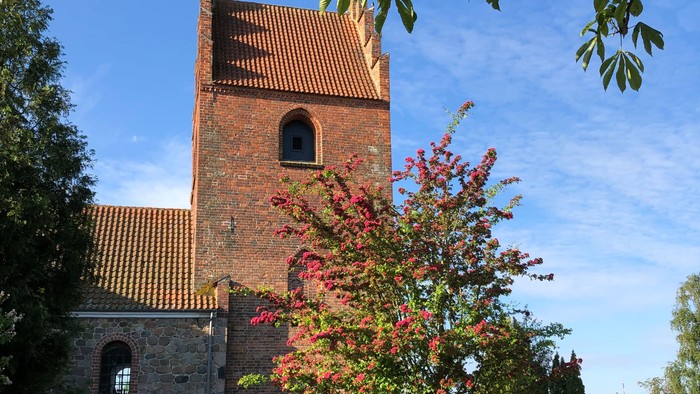 En gammel kirke med tårn og murvej ved en grøn plads