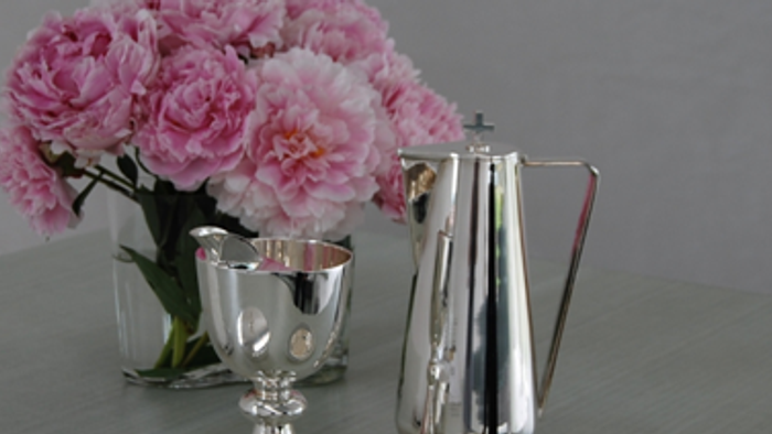 En sølv tekanne og tegnabod med rosa blomster i en vase på bordet