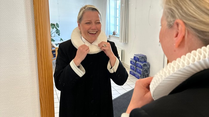 En kvinde tager et selfie for et spejl, mens hun smiler og holder en telefon.