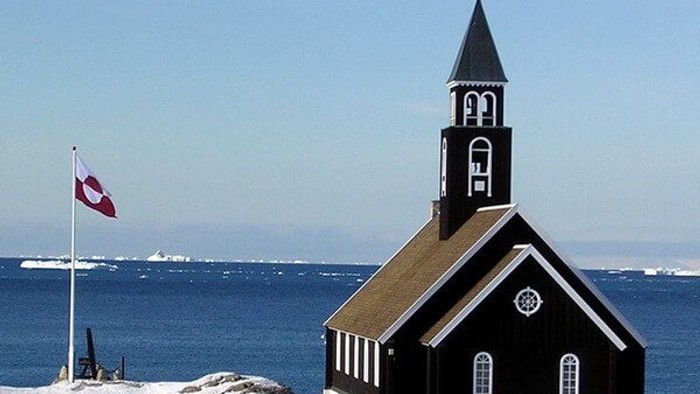 Sort kirke ved havet med dansk flag.