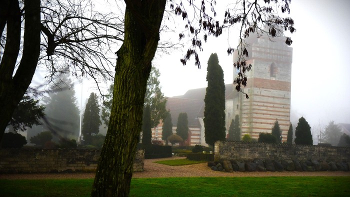 Tåget landskab med et højt tårn omgivet af løvfældende træer og et roligt haveområde.